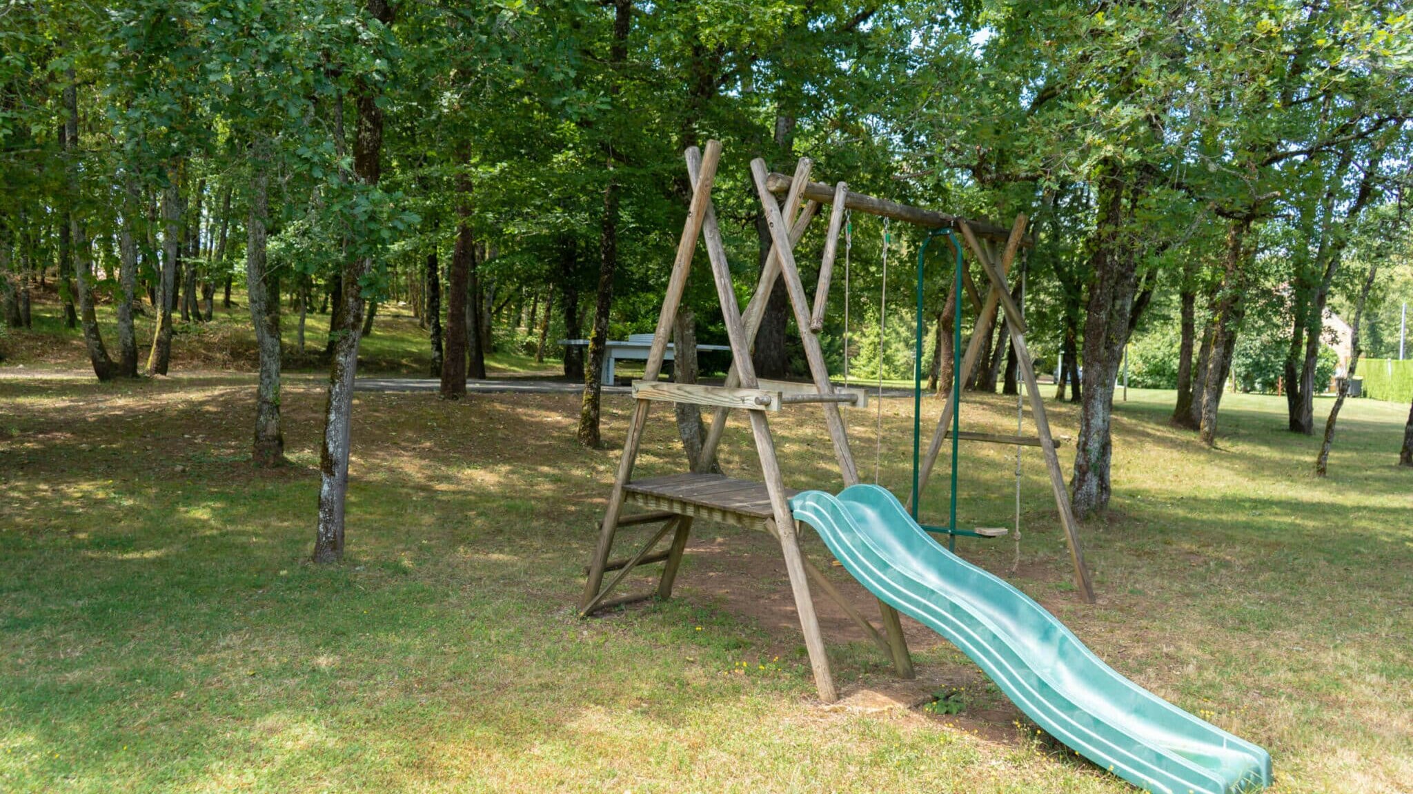 Jeux pour enfants avec toboggan, balançoire et table de ping pong en arrière plan dans le terrain du grand gîte du Clos des Aubiers