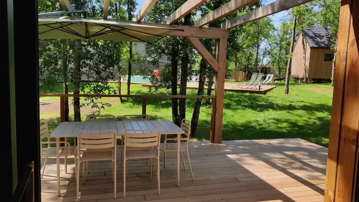Terrasse avec parasol, table et chaises proche de la piscine du gîte la Clairière des Aubiers
