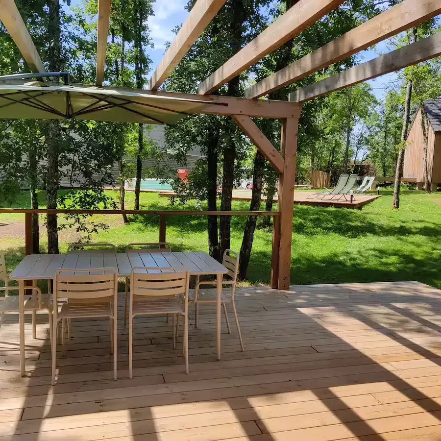 Terrasse avec parasol, table et chaises proche de la piscine du gîte la Clairière des Aubiers